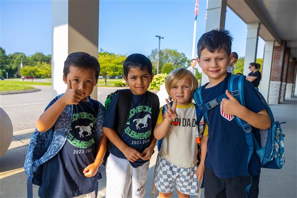 four boy students giving thumbs up and peace signs